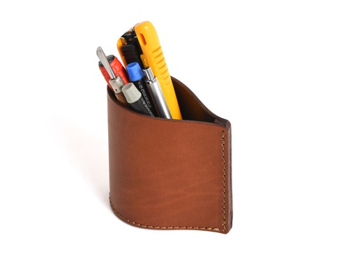 職人手作皮革筆筒，採用棕色皮革製成，設計簡潔，可收納多支筆及工具，例如黃色美工刀、螺絲起子和筆。