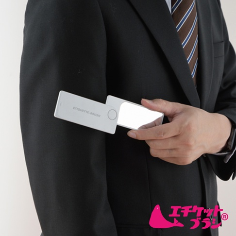 白色可折疊隨身衣物除塵刷，刷身印有「ETIQUETTE. BRUSH」字樣，搭配可伸縮的鏡面，由穿著黑色西裝的男士手持，展示其便攜性。