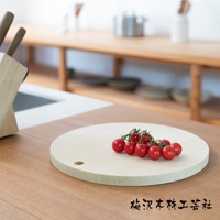 淺色木質圓形砧板，直徑約 30 公分，一側有掛孔，上面放著一串紅色的聖女番茄。