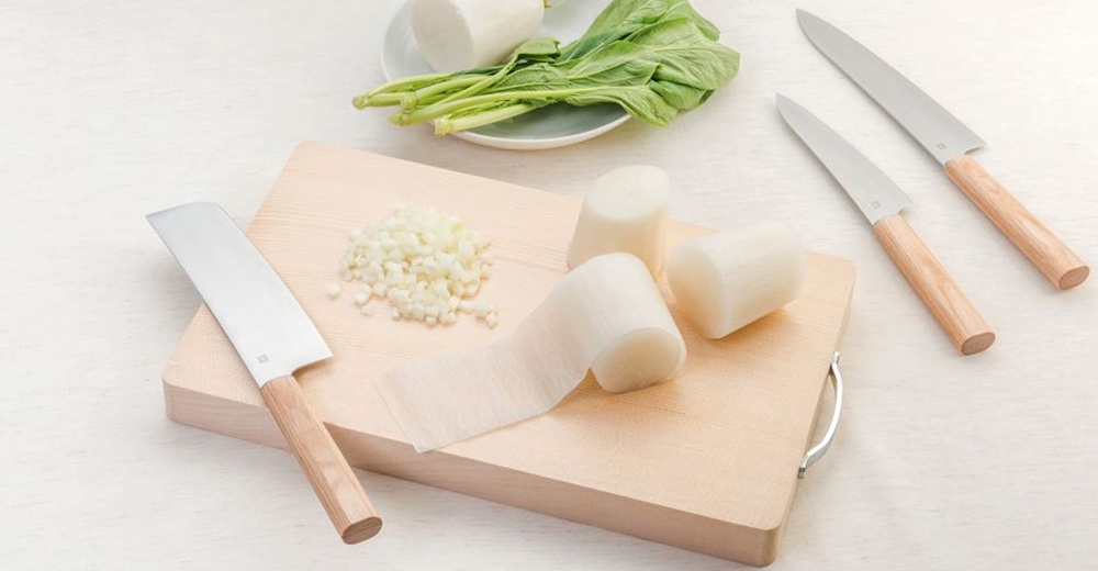 Yuri / Petit knife 水果刀，刀刃採用銀色金屬材質，搭配淺木色刀柄。產品包含一把寬刃刀和兩把細長刀，置於淺色木製砧板上，旁邊有切塊的白蘿蔔、切碎的洋蔥和一小撮綠葉蔬菜。