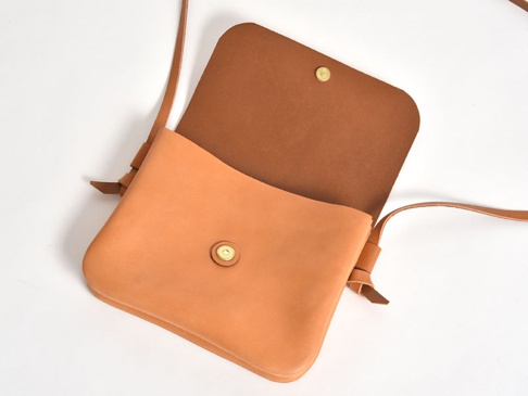 職人手作皮革橫式隨行袋，淺棕色皮革製成，翻蓋設計，配有金屬按扣和細長肩帶。
