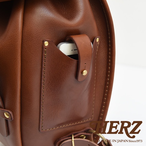職人手作皮革經典雙扣後背包 R-152，採用棕色皮革，設有外側手機袋，以粗線縫製，風格經典。