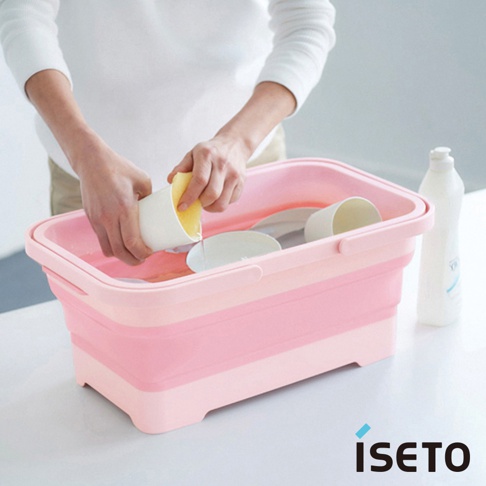 粉紅色和淺粉色雙層伸縮提籃，內有白色杯子、盤子，有人手持海綿清洗杯子，提籃兩側有提把，背景有白色清潔劑瓶。