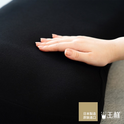 一隻手輕柔地觸碰著黑色的枕套，布料帶有細緻的紋理。右下角有「日本製造 原裝進口」及「王樣」的品牌標誌。