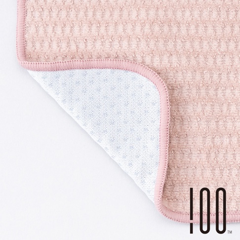 一塊淺粉色的降溫涼感毛巾，材質柔軟，表面有格紋紋理。毛巾一角被掀起，露出內側白色網狀織物，織物上有規則排列的藍色小圓點。毛巾邊緣以同色系的粉色滾邊處理。