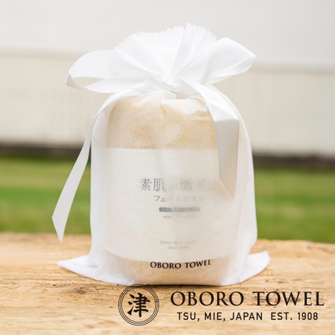 白色網狀包裝袋內，裝著一疊米黃色、帶有細緻紋理的毛巾，袋口以白色緞帶綁成蝴蝶結，包裝上有日文「素肌の潤」、「フェイスタオル」及英文「bare skin tender」、「FACE TOWEL」等字樣，底部印有「OBORO TOWEL」品牌名稱。