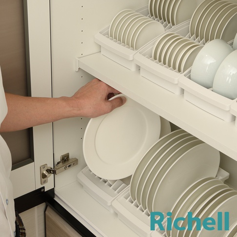 櫥櫃式餐盤收納架由白色塑膠製成，內有兩個白色餐盤架，分別收納著白色和淺灰色的盤子，左側有一隻手正在從架子上拿起一個白色盤子。