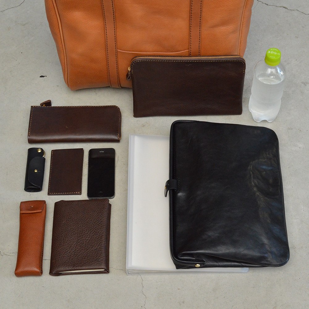 職人手作皮革Organ肩背拉鍊托特包 G-58，包含一個橘棕色皮革托特包、一個深棕色拉鍊長夾、一個黑色拉鍊手拿包、一個橘棕色筆套、一個深棕色筆記本、一個黑色手機、一個深棕色卡夾、一個黑色皮革平板電腦保護套，以及一瓶水。