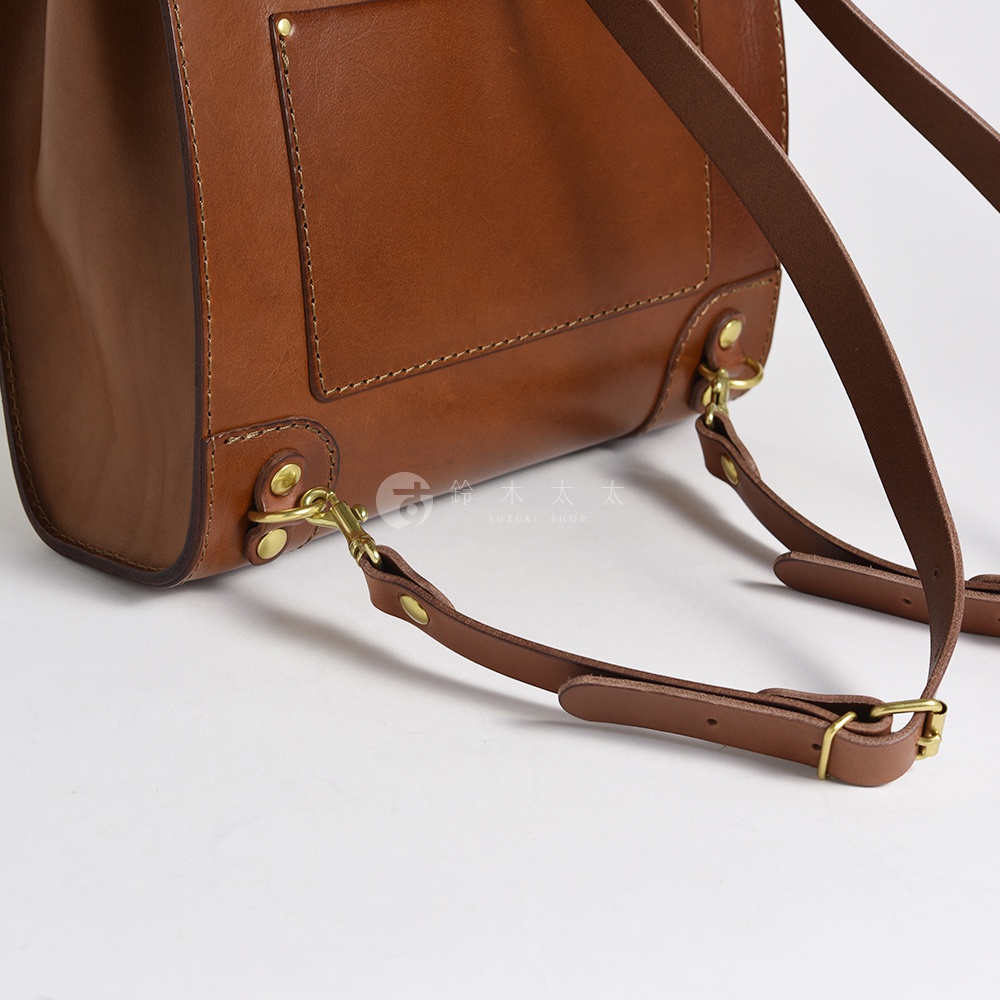 職人手作皮革復古口金後背包，採用溫暖的棕褐色真皮材質，搭配復古黃銅色五金扣環和調節帶，展現精緻工藝與經典風格。
