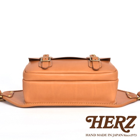 職人手作皮革騎士隨身斜背包，淺棕色天然皮革材質，雙扣帶翻蓋設計，側面有金屬鉚釘固定。