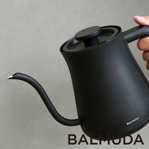 黑色霧面手沖壺，配有細長彎曲壺嘴和圓形壺蓋，手柄處有 BALMUDA 品牌標誌。