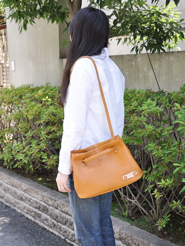 淺棕色皮革製成的兩用托特包，有可調式肩帶，包身縫線明顯，右側有品牌標籤。