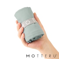 手持一個摺疊起來的薄荷綠色環保隨行袋，袋子由輕薄材質製成，並用灰色束帶固定，束帶上印有白色「MOT」字樣。