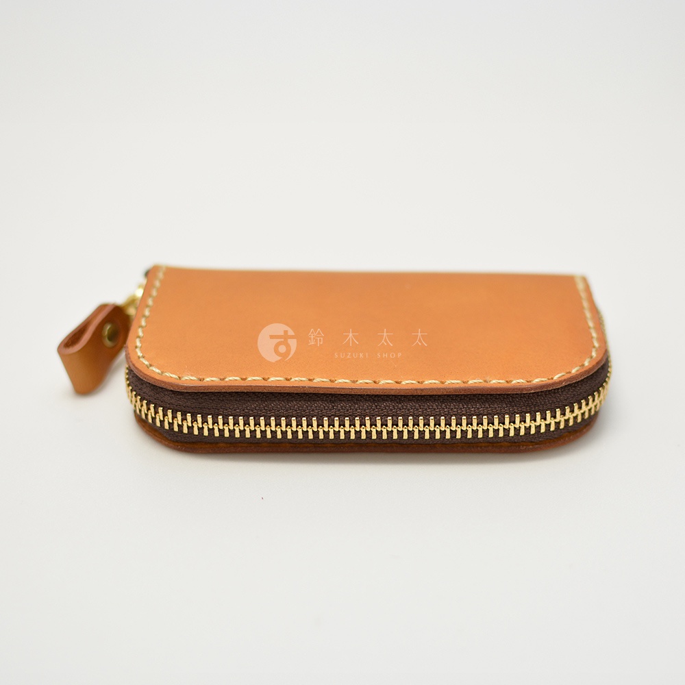 職人手作皮革橢圓形拉鍊鑰匙包，咖啡色皮革搭配金色拉鍊，左側有皮革拉繩，包面上印有SUZUKI SHOP標誌。