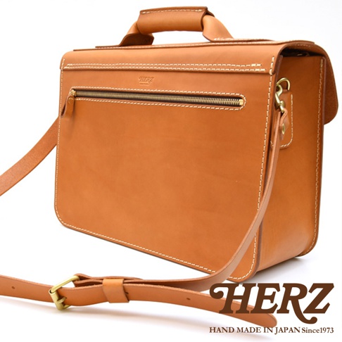 職人手作皮革經典雙扣兩用單肩包，採用天然棕色皮革，配有銀色拉鍊、金色調節扣和肩帶。包款設計簡約，縫線清晰，展現精湛工藝。