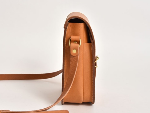 職人手作皮革翻蓋迷你單肩包，採用天然棕色皮革製作，帶有可調節的肩帶和金屬扣環，設計簡潔實用。