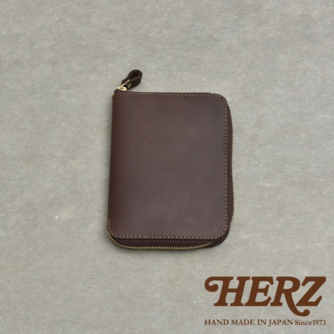 深棕色皮革製成的拉鍊式記事本收納包，附有小提把，背景為灰色紋理桌面。