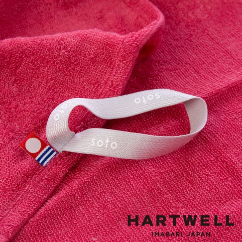 粉紅色毛巾特寫，毛巾材質細緻，繡有soto字樣的白色掛繩，角落有品牌標誌。