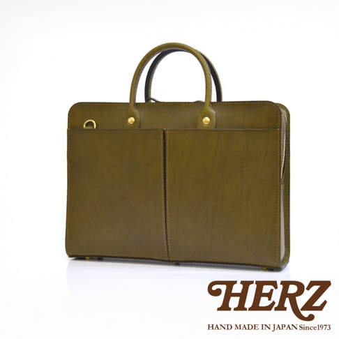 橄欖綠皮革雙口袋兩用商務公事包，設有兩個前袋、頂部提把、金色金屬拉鍊及 D 型環，展現職人手作質感。