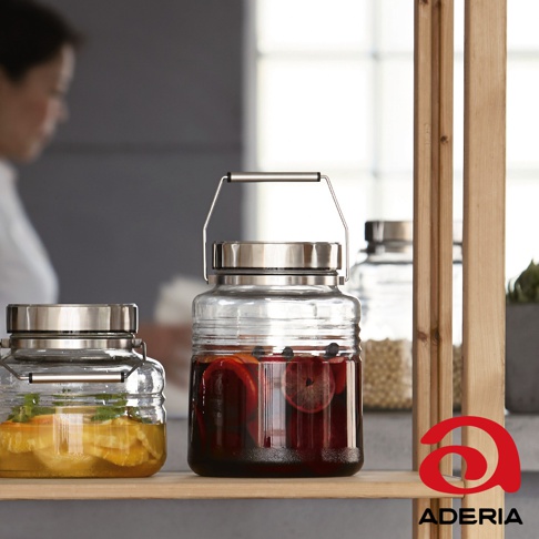 兩個透明玻璃罐，一個裝有水果和香草，另一個裝有深紅色液體和水果片，均配有銀色不鏽鋼蓋和提把，擺放在木架上。