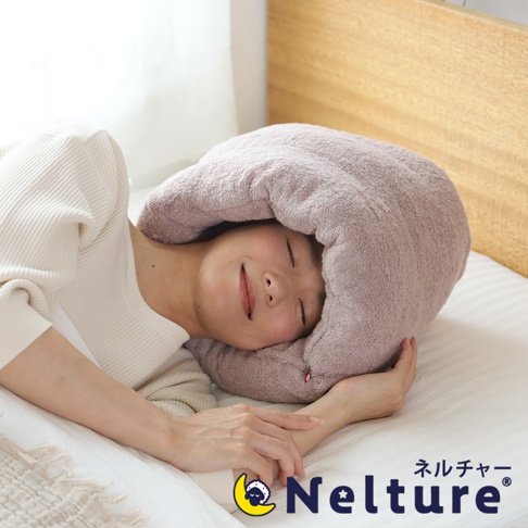 一位女士躺在床上，頭部被一個柔軟的粉色毛巾枕包覆，枕頭呈現甜甜圈狀，材質看起來蓬鬆舒適，營造出安穩的睡眠氛圍。