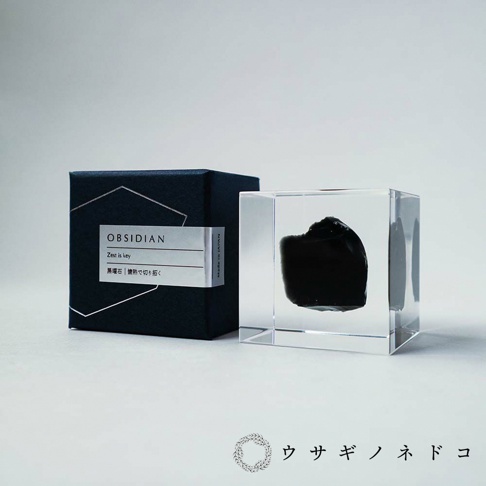 Sola cube Mineral礦石立方塊，內含一塊黑色不規則黑曜石，置於透明立方體中。產品旁有一深藍色禮盒，盒蓋印有「OBSIDIAN」字樣及日文說明。