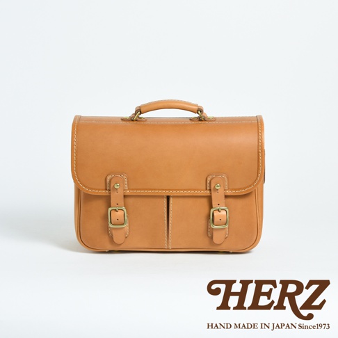 經典棕色皮革製成，具有手提把、兩個前袋和金色搭扣。此款包包線條俐落，風格復古，適合商務或休閒場合使用。