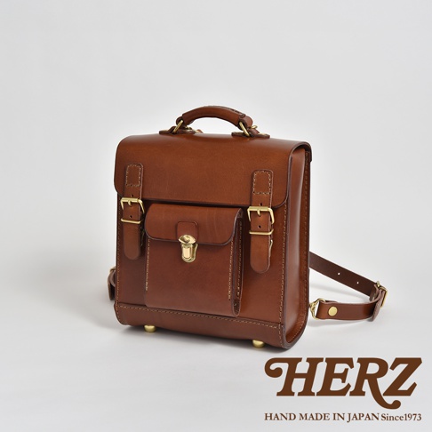 職人手作皮革經典學院風迷你後背包，呈現棕褐色，帶有可調節的肩帶、金屬扣環和掀蓋式前袋。