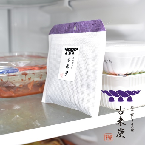 白色網狀織物袋裝著古來炭，上方有紫色紙質吊牌，袋身印有黑色日文文字與圖案。旁邊有透明塑膠盒裝著食物，以及白色波浪紋塑膠容器。