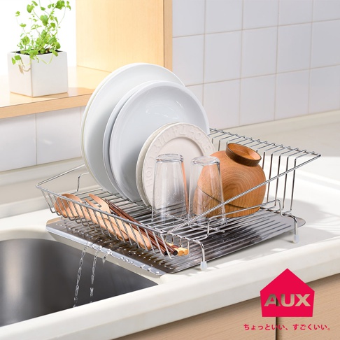 不鏽鋼方形瀝水籃，置放著白色盤子、玻璃杯及木製碗，排水孔流出水滴。