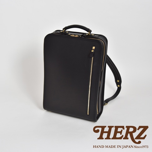 職人手作皮革商務電腦後背包 R-25，黑色。方形包體，材質為光滑皮革，配有金色拉鍊和提把，側面有雙肩帶。