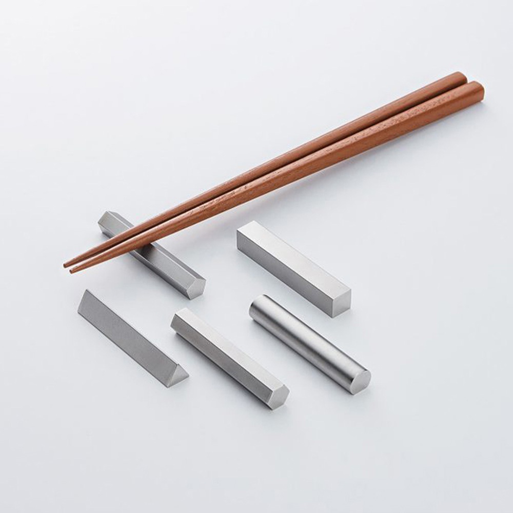 一雙木質筷子架在幾個金屬製成的幾何形狀筷架上，包括長方形、六角形和三角形，呈現銀灰色調。