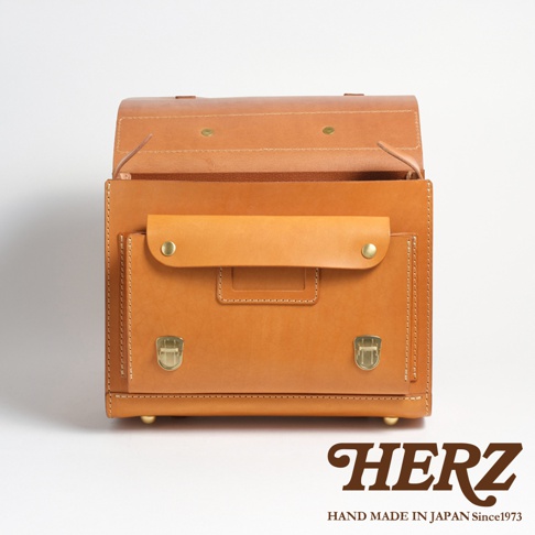 職人手作皮革橫式書包，自然光澤的淺棕色皮革，正面有翻蓋口袋和金屬鎖扣，整體風格簡約復古。