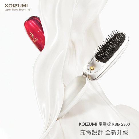 KOIZUMI 負離子音波磁氣美髮梳 KBE-G500，充電式設計，主體為白色，搭配紅色磁性梳柄，梳面為黑色，金屬梳針，置於白色絲綢布料上。