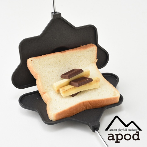 黑色鑄鐵材質的熱壓三明治烤夾，上面放有一片吐司，吐司上疊著香蕉切片和巧克力塊。