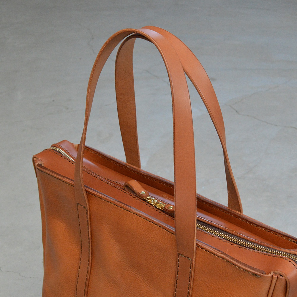 職人手作皮革Organ肩背拉鍊托特包，採用天然棕色皮革，配有金色拉鍊和提把，設計簡潔實用。