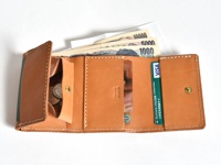 職人手作皮革三折式迷你短夾，淺棕色皮革，內有日圓紙鈔、硬幣、信用卡及其他卡片，縫線清晰。
