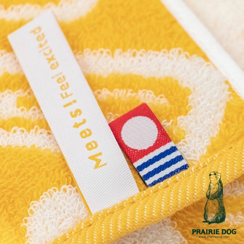 黃色提花方巾，上面有白色和黃色條紋，一條白色標籤上印有橘黃色字體 meets! feel excited。