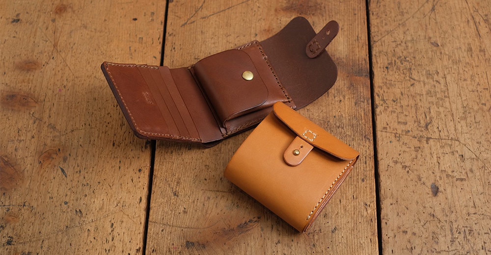 職人手作皮革原子釦型二折式短夾，展示棕色與淺棕色兩款，皮革材質，簡約設計。