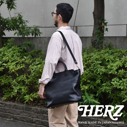 黑色皮革兩用托特包，配有可調節肩帶，包身線條流暢，底部設有金屬腳釘。