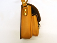 側視圖，職人手作的黃褐色皮革直式單肩包，附有金屬釦和皮革翻蓋。