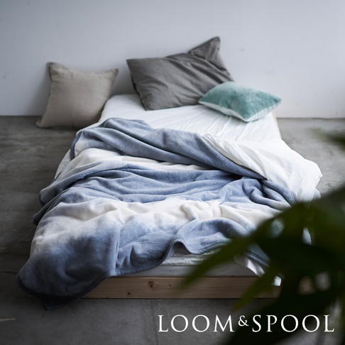 Flood of Light 抗菌短絨舒柔單人毯，採用柔軟的短絨材質，呈現藍白色漸層設計，鋪陳於床鋪上，旁邊擺放數個不同顏色與質感的抱枕。