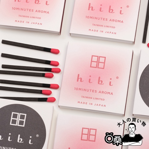 多個粉色漸層包裝盒，盒上印有「hibi 10MINUTES AROMA TAIWAN LIMITED MADE IN JAPAN」字樣及圖案。旁邊擺放著數支黑色木質火柴，頂端有紅色火藥頭。