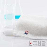 一條柔軟的白色今治超長棉浴巾，帶有紅色標籤，上面有藍色條紋和圓形圖案。背景是模糊的實驗室燒杯，裡面裝有藍色液體。