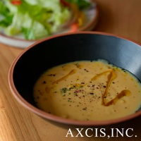 PURE 素燒百搭陶瓷沙拉碗，內裡為黑色，外緣帶有陶土原色，碗中盛有濃稠的黃色湯品，表面淋有橄欖油並撒有香草和黑胡椒粒。