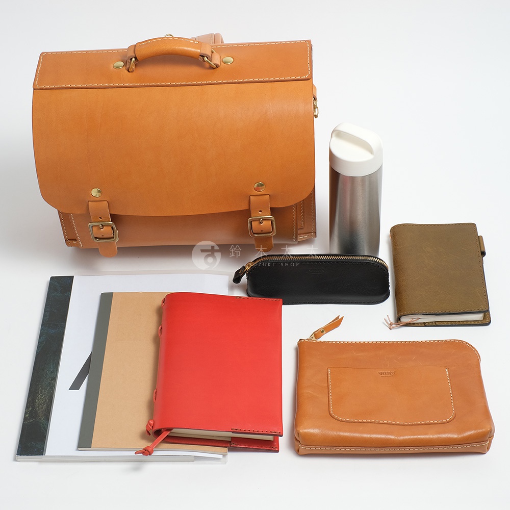 一個裝有筆記本、筆袋、保溫瓶和皮革包的組合，其中皮革包為橫式設計，有兩個皮帶扣。