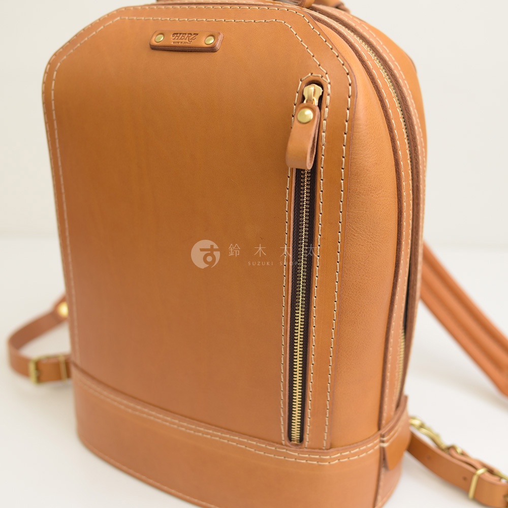 職人手作的棕色皮革立體商務後背包，設有金色拉鍊和精緻縫線，材質為天然皮革。