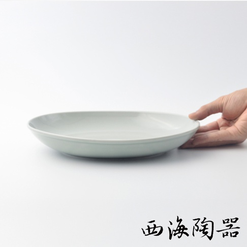 波佐見燒 Common 陶瓷橢圓餐盤，淺灰藍色，直徑 27 公分，由陶瓷製成，盤身呈現柔和曲線，一只手輕扶盤緣。