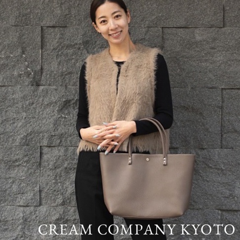 一位女性手持一個淺棕色皮革托特包，包包款式簡潔，配有雙提把。