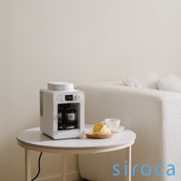 白色SC-A3520自動研磨咖啡機，搭載黑色玻璃咖啡壺，置於白色圓形桌上，旁邊有一杯咖啡和司康餅。